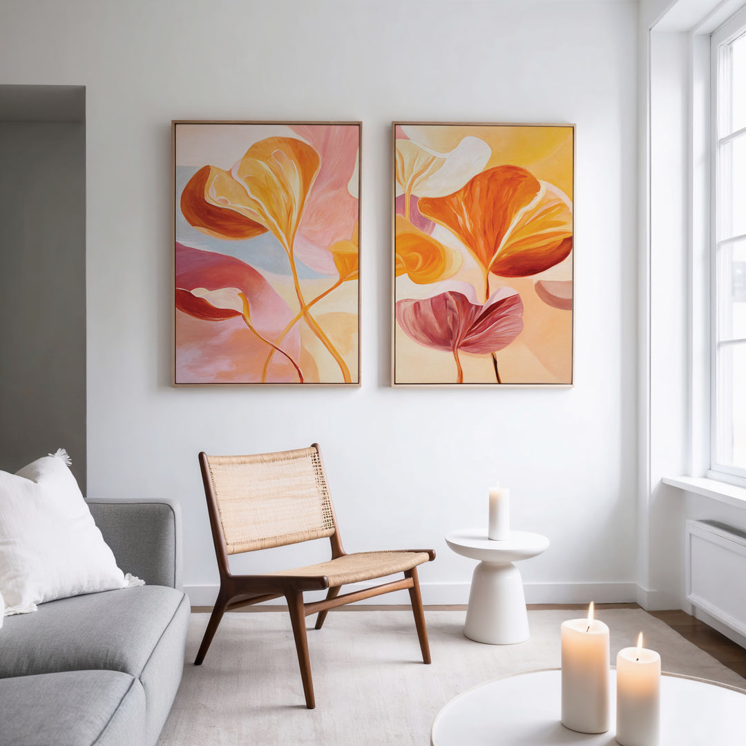A modern living room with a light gray sofa, wooden chair with woven seat, small round side table, and three lit candles. Above the chair, the Autumn Reverie - Set of 2 botanical wall art brightens the white wall.