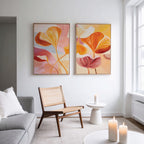 A modern living room with a light gray sofa, wooden chair with woven seat, small round side table, and three lit candles. Above the chair, the Autumn Reverie - Set of 2 botanical wall art brightens the white wall.