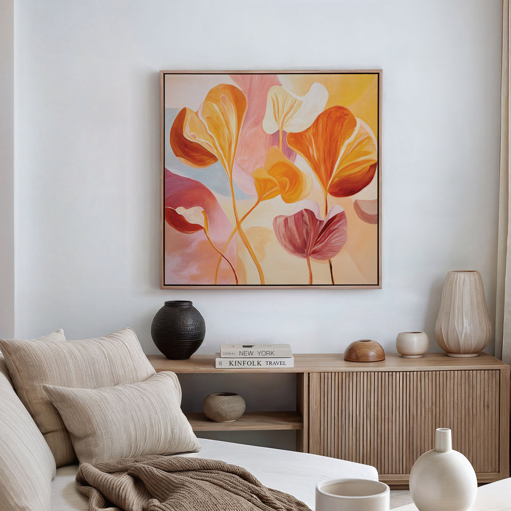 A cozy living room with neutral furniture, vases, and books features the Autumn Reverie Canvas Art - Square: an abstract floral print in red, orange, and pink displayed above a wooden console on a white wall.