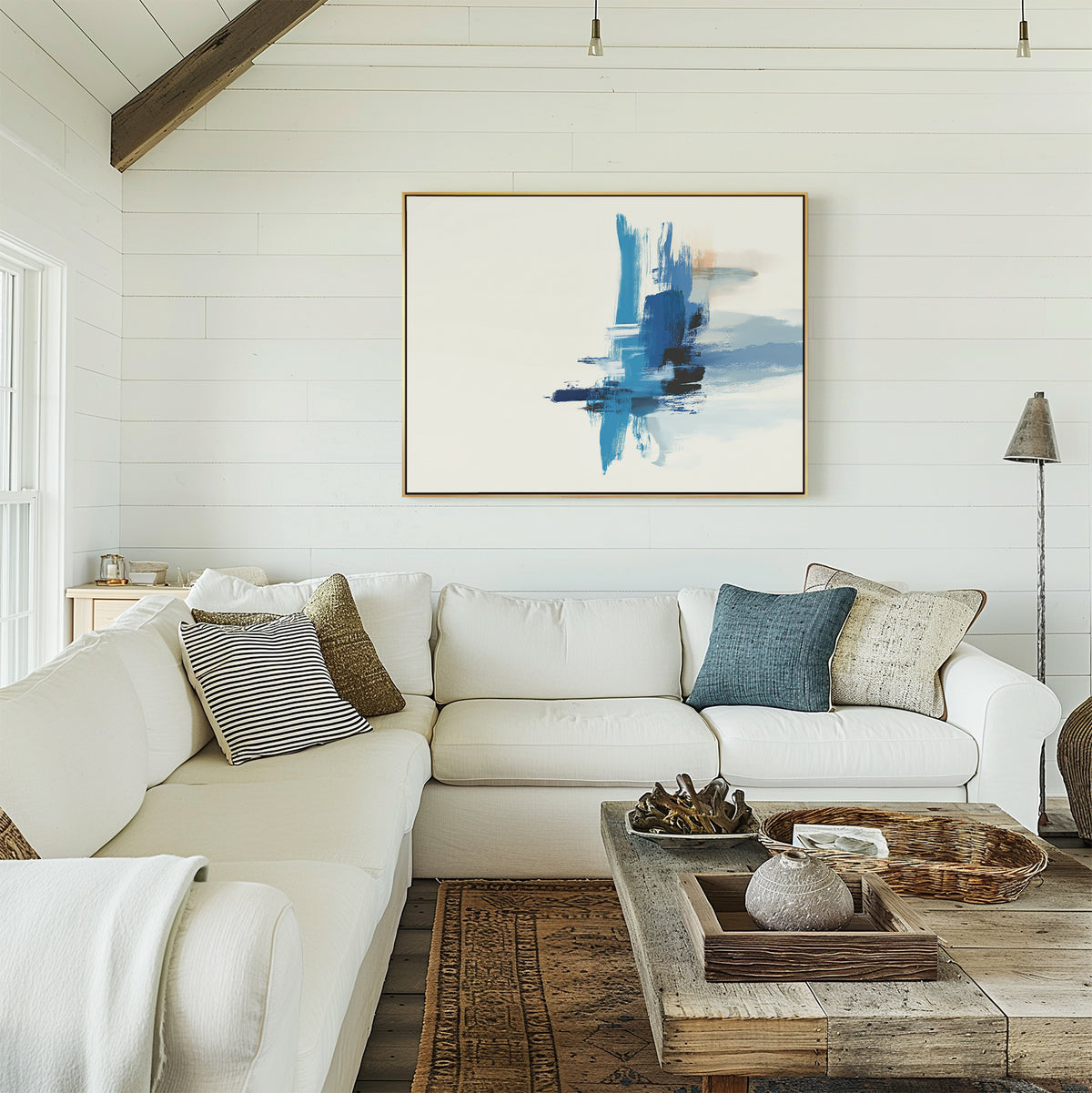 A bright living room features a white sectional sofa, assorted pillows, and a rustic wooden coffee table. The Azure Convergence Canvas Art - Horizontal hangs above the couch on the white shiplap wall as modern decor.