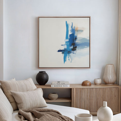 Minimalist living room featuring a beige sofa, neutral pillows, a wooden sideboard with vases and books, and the Azure Convergence Canvas Art - Square as striking modern wall art above the seating area.