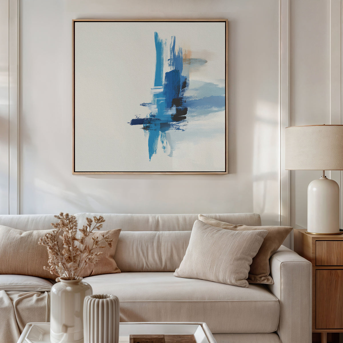 A modern living room with a beige sofa, neutral pillows, a white lamp, and dried flowers on the coffee table. The Azure Convergence Canvas Art - Square is framed and displayed above the couch as contemporary wall art.