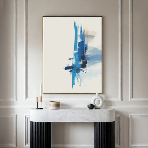 The Azure Convergence Canvas Art - Vertical, featuring bold blue brushstrokes, hangs on a light wall above a marble console table adorned with two candles, a black bowl, and a white circular sculpture.