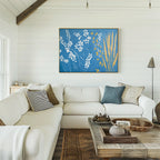 A cozy living room features a white sectional, textured pillows, a wood coffee table with decor, and the Azure Meadow Canvas Art - Horizontal as striking botanical wall art on a white shiplap wall. Sunlight streams in from windows on the left.