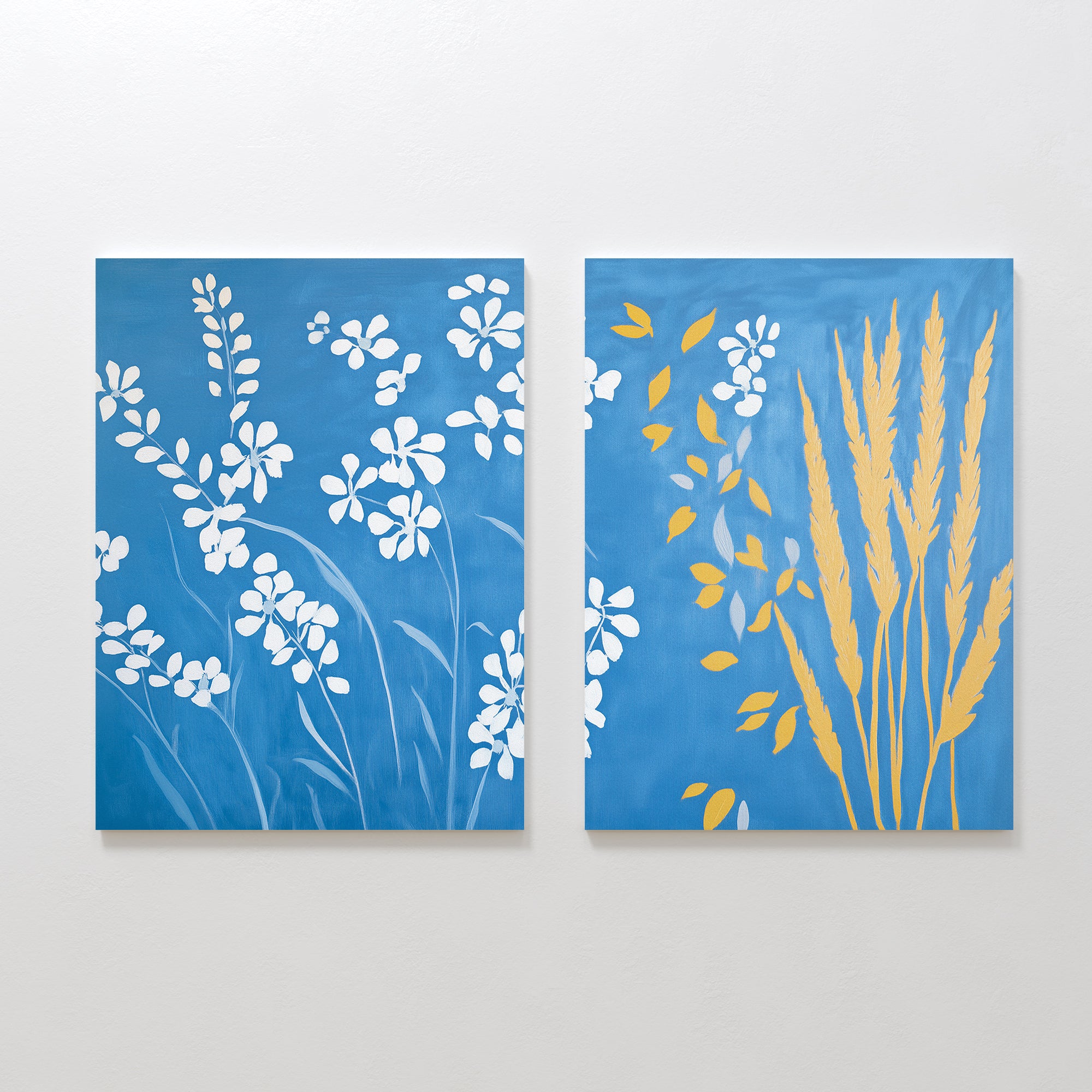 The Azure Meadow - Set of 2 features blue canvases: the left shows white wildflower silhouettes, while the right displays yellow wheat and leaf shapes with some white flowers on the left—bringing serene meadow vibes to your space.