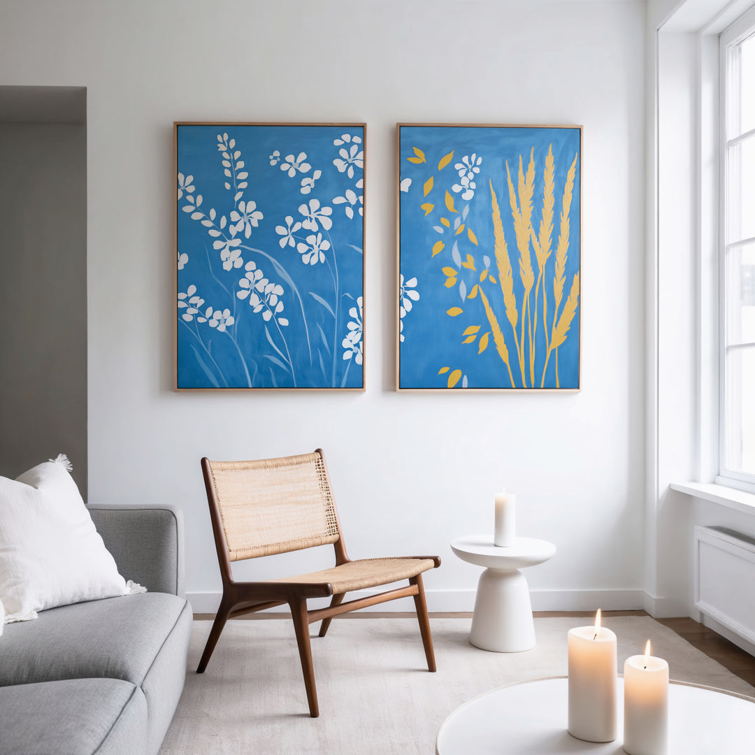 A modern living room with a light gray sofa, wooden chair, and white side table. Candles and large windows create a peaceful vibe, while the Azure Meadow - Set of 2 canvas prints featuring white wildflowers add charm above.
