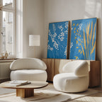 A modern living room with two white, rounded chairs, a low wooden coffee table, and a light wood sideboard. The Azure Meadow - Set of 2 featuring white wildflowers adds charm as sunlight streams through tall windows onto the Nordic Park-inspired decor.