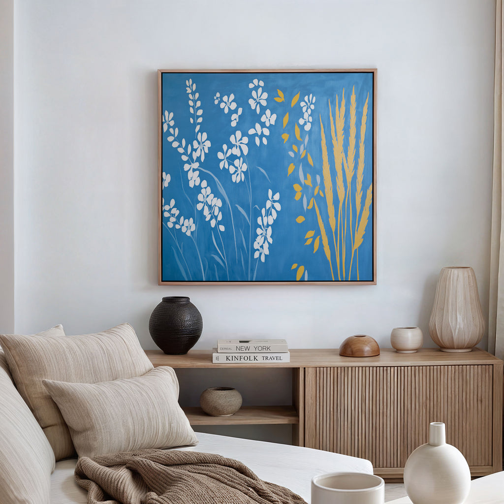 A modern living room with neutral-toned furniture, showcasing the Azure Meadow Canvas Art - Square above a wooden sideboard decorated with vases, a bowl, and stacked books.