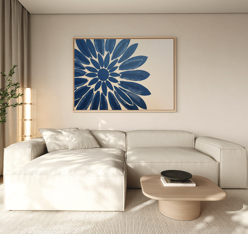 A modern living room features a light beige sectional, low wood coffee table, and the Azure Radiance Canvas Art - Horizontal, showcasing a blue abstract flower. Neutral tones and natural light add to the calm, minimalist vibe.