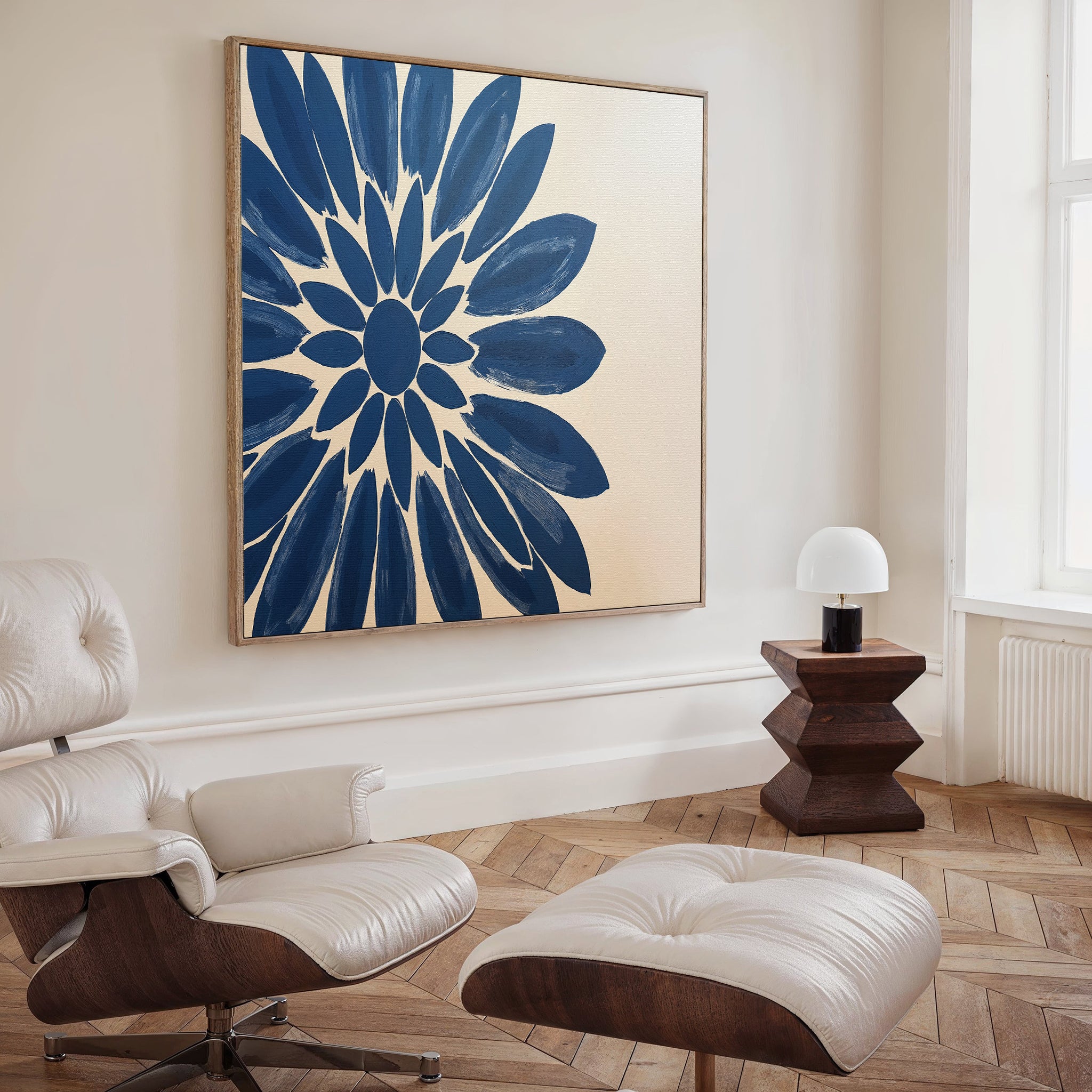 A modern living room with a light-colored lounge chair and ottoman, a wooden side table with a small white lamp, and the Azure Radiance Canvas Art - Square above a herringbone wood floor—perfect for elevating your decor.