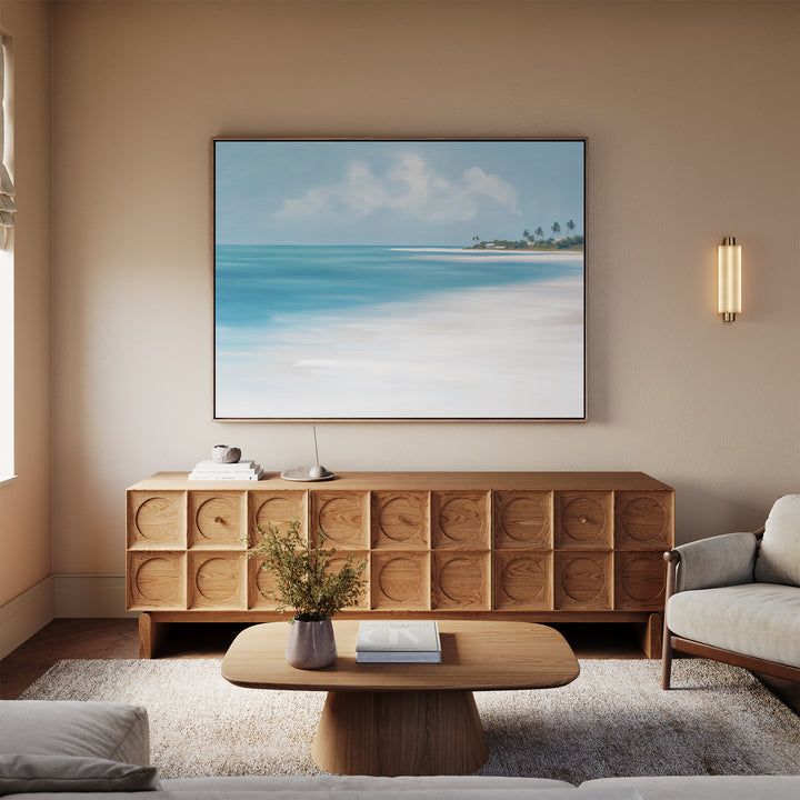 A cozy living room with a light wood sideboard, low coffee table, and beige sofa. The Azure Tranquility Canvas Art - Horizontal hangs above, while a small plant sits on the table. Décor is minimalist in neutral tones.