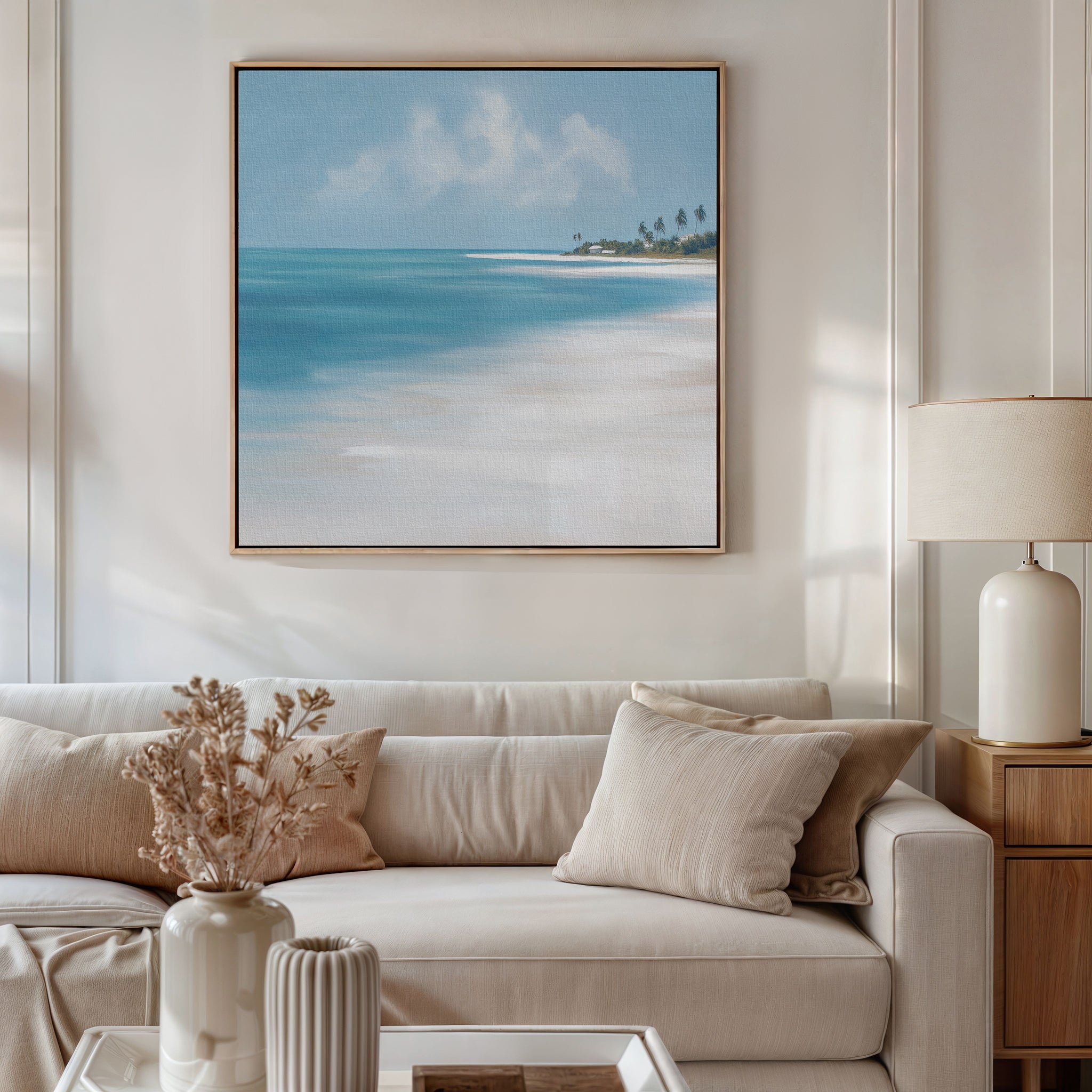 A cozy living room with a beige sofa, neutral pillows, and a side table with a lamp is accented by vases of dried flowers. The Azure Tranquility Canvas Art - Square hangs above the sofa, adding relaxing coastal vibes to the space.