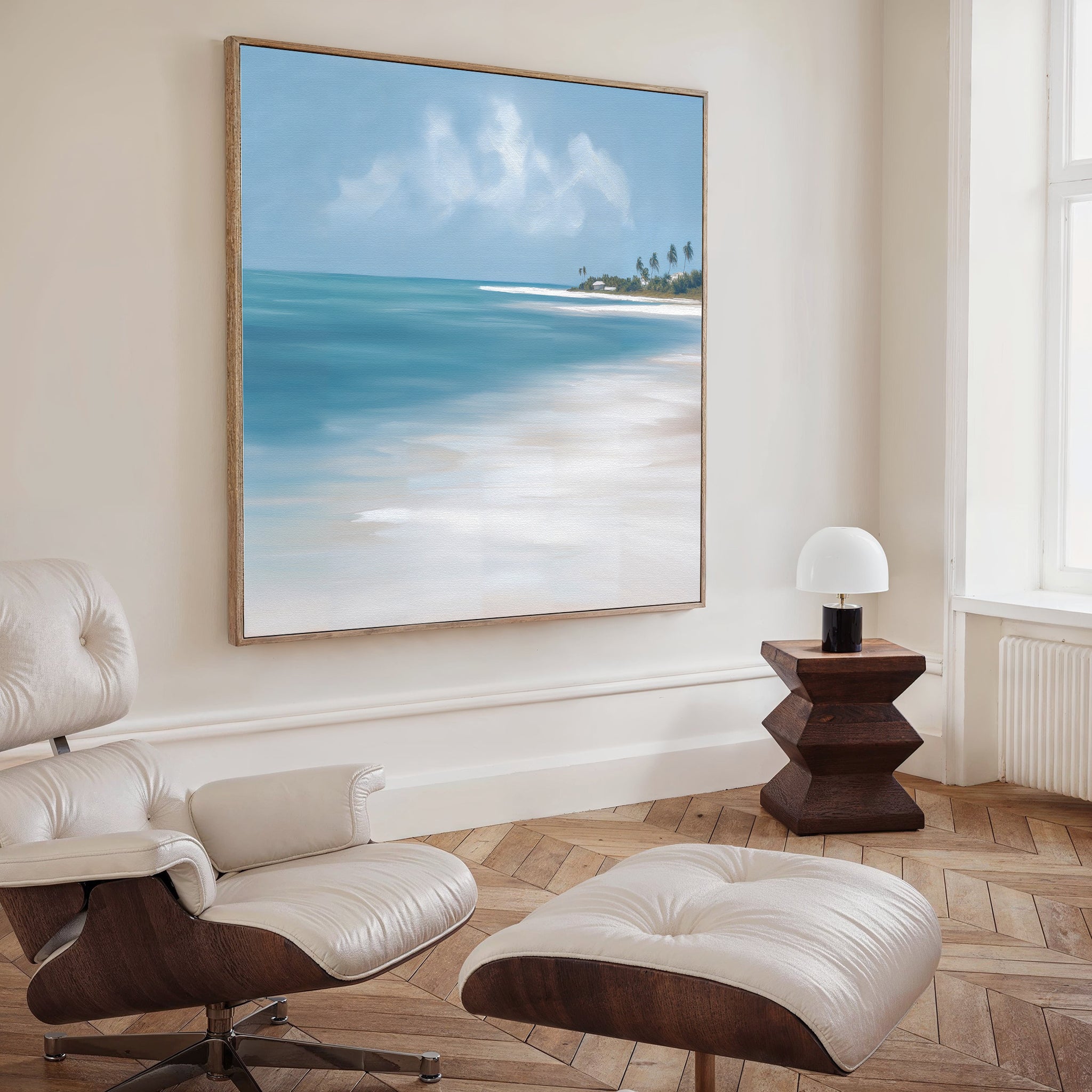 A modern living room with a white leather lounge chair and ottoman, a wooden side table with a white lamp, and the Azure Tranquility Canvas Art - Square featuring serene turquoise waters displayed on the wall.