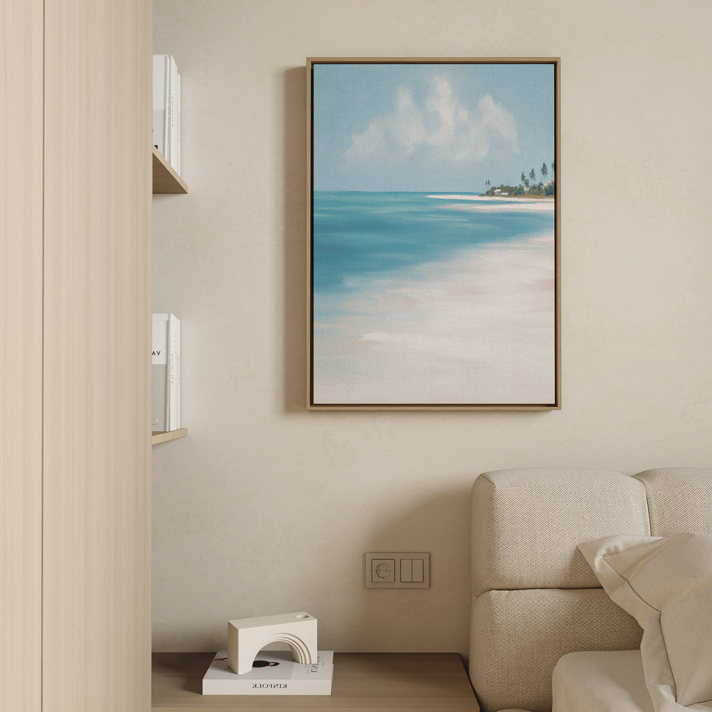 The Azure Tranquility Canvas Art - Vertical, featuring turquoise waters and a sandy shore, is framed and displayed on a beige wall above a light sofa in a modern, minimalist living room. A shelf with books and decor sits nearby.