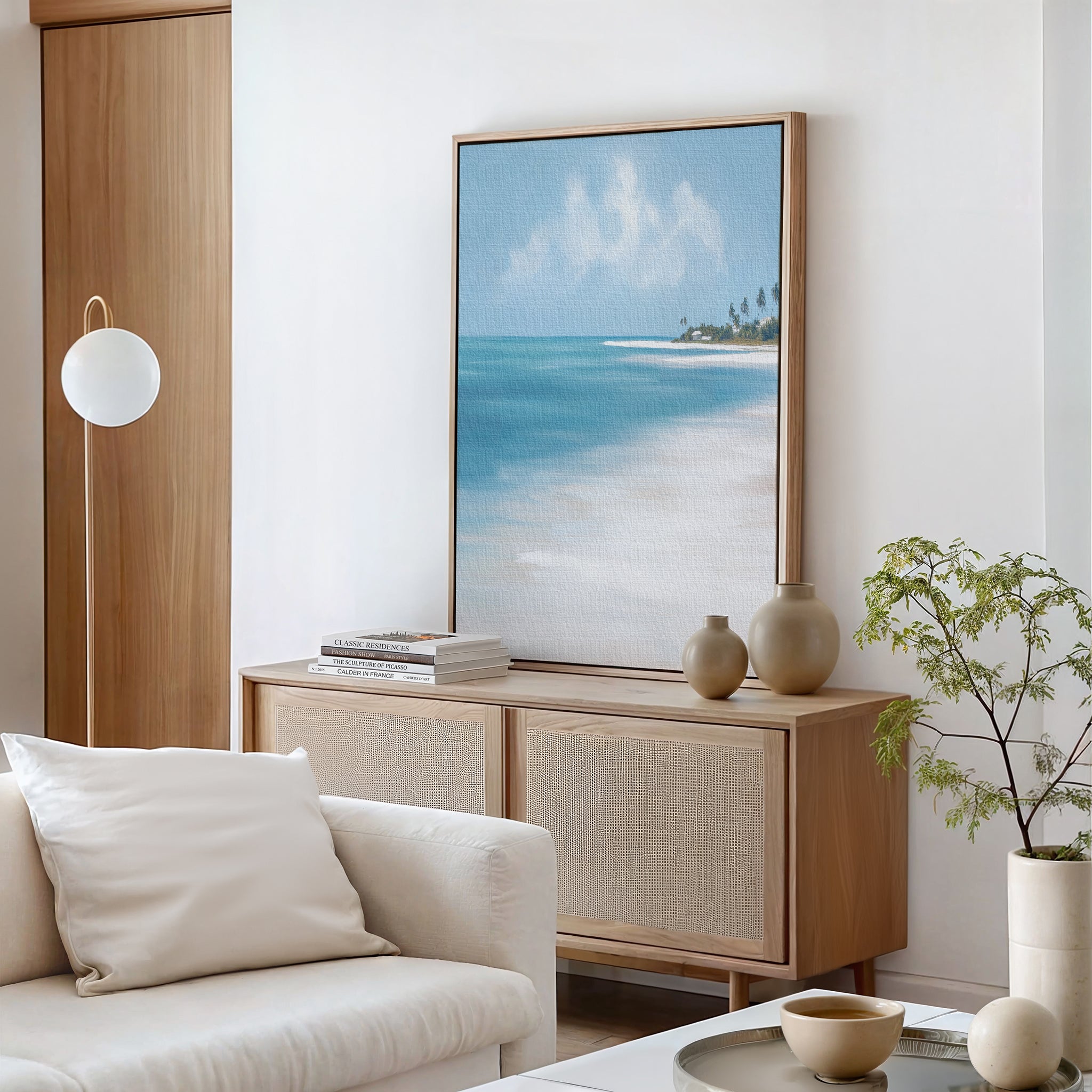 A bright, modern living room with a light wood cabinet, neutral decor, a potted plant, and the Azure Tranquility Canvas Art - Vertical featuring turquoise waters and distant palm trees for serene wall art.