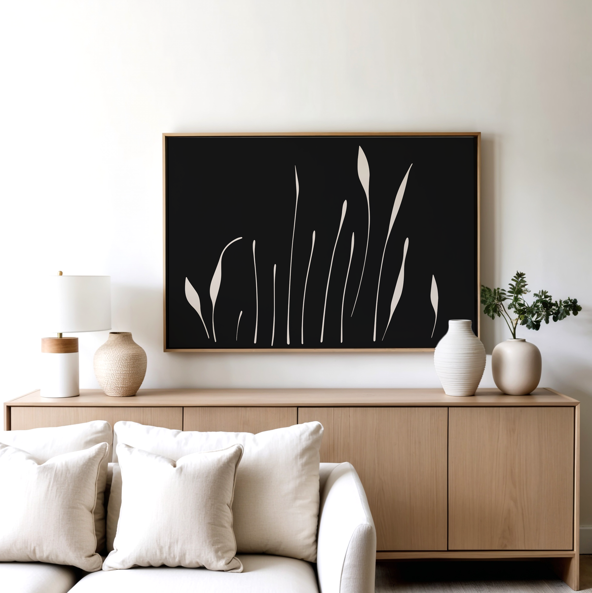 A modern living room features a light wood sideboard, white vases, a table lamp, and the Botanical Silhouettes Abstract Canvas Art above a beige sofa with white cushions.
