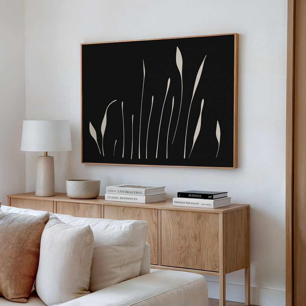 A modern living room features a light wood sideboard, white table lamp, ceramic bowl, stacked books, and Botanical Silhouettes Abstract Canvas Art with plant-like shapes above. A cream-colored sofa is in the foreground.