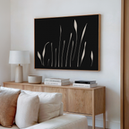 A modern living room features a light wood sideboard, white table lamp, ceramic bowl, stacked books, and Botanical Silhouettes Abstract Canvas Art with plant-like shapes above. A cream-colored sofa is in the foreground.