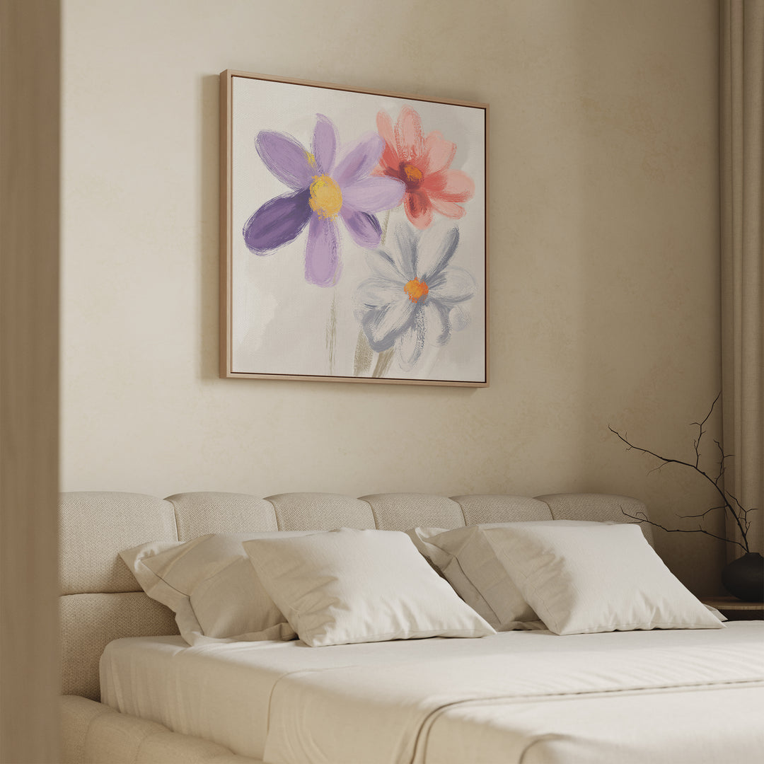 A neutral bedroom features a cream bed with four white pillows. Above the bed hangs the Blooming Harmony Canvas Art - Square, showcasing three large flowers in purple, pink, and light blue tones on a white background.