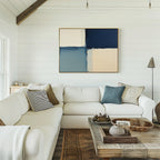 A bright living room features a white sectional sofa, textured pillows, a rustic wood coffee table, neutral décor, and the Blue Quarters Canvas Art - Horizontal with navy, blue, and cream blocks on a white shiplap wall—ideal for modern spaces.