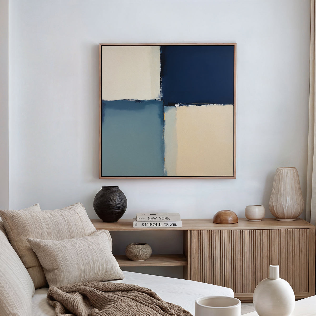 A modern living room features a beige sofa, striped pillows, wooden sideboard, decorative vases, books, and the Blue Quarters Canvas Art - Square in cream, blue, and navy as a striking focal point above.