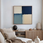 A modern living room features a beige sofa, striped pillows, wooden sideboard, decorative vases, books, and the Blue Quarters Canvas Art - Square in cream, blue, and navy as a striking focal point above.