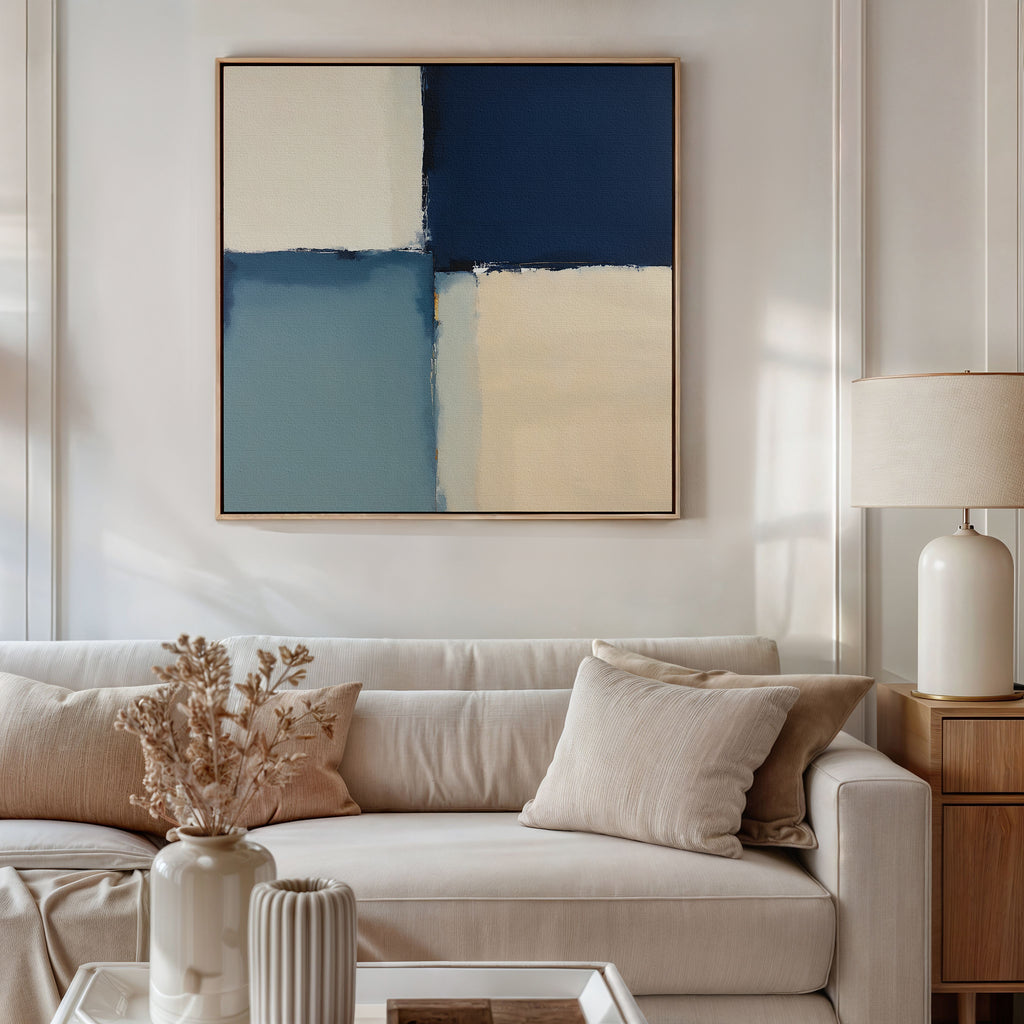 A modern living room with a beige sofa, neutral cushions, dried flowers in a vase, a table lamp, and the Blue Quarters Canvas Art - Square featuring navy, light blue, and cream geometric blocks above the sofa.