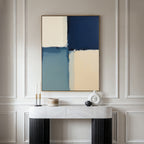 A modern console table with decorative objects sits against a paneled wall, topped by the Blue Quarters Canvas Art - Vertical, featuring a blue, cream, and beige geometric design—an ideal accent for modern living rooms.