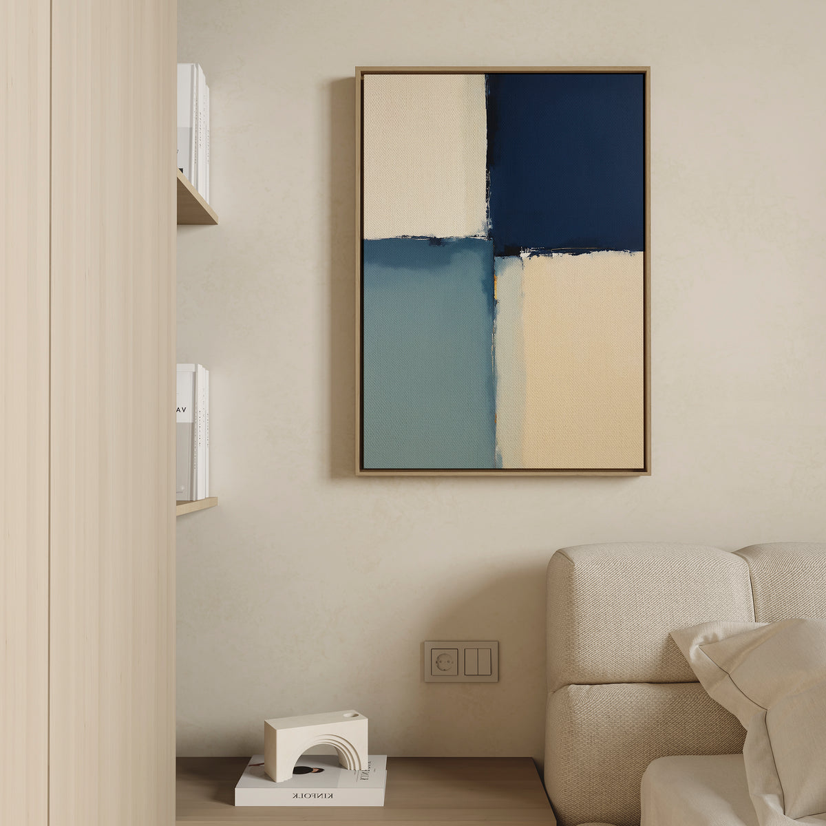 A modern living room features a beige sofa, light wood shelves with books, and the Blue Quarters Canvas Art - Vertical in blue, cream, and beige tones hanging above a small white sculpture and electrical outlets.