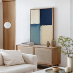 A modern living room with a light wood sideboard, Blue Quarters Canvas Art - Vertical in blue and beige tones, decorative vases, a small potted plant, and a white couch with a cushion. Minimalist decor in neutral colors.