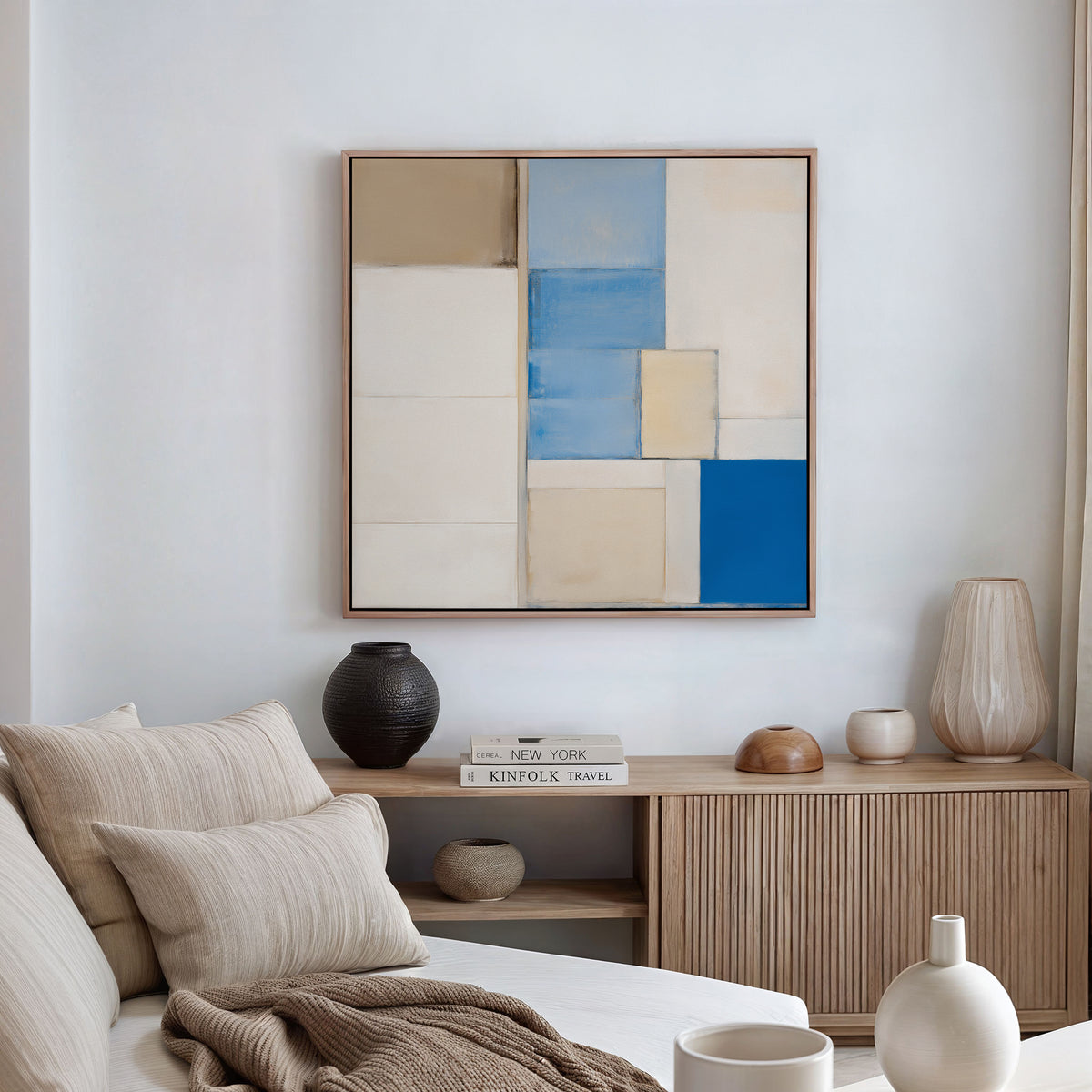 A modern living room featuring a neutral sofa, beige and cream cushions, a wooden sideboard with decor, and the Blue Tiles Composition Canvas Art - Square as striking geometric wall art—ideal for lovers of modern decor.