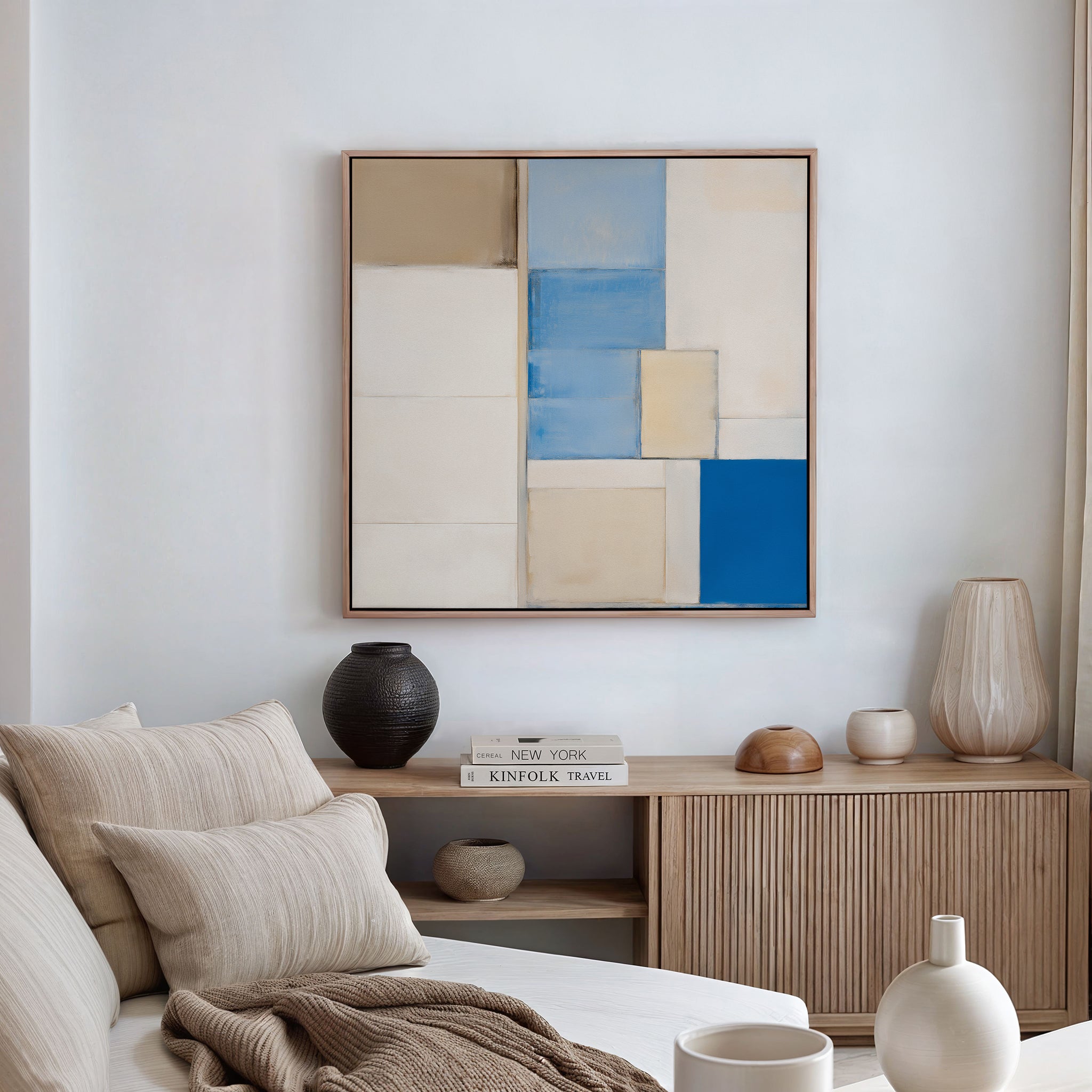 A modern living room featuring a neutral sofa, beige and cream cushions, a wooden sideboard with decor, and the Blue Tiles Composition Canvas Art - Square as striking geometric wall art—ideal for lovers of modern decor.