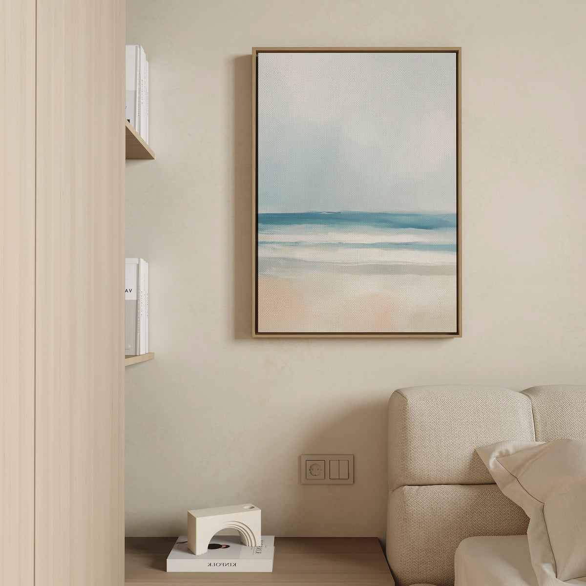 The Blurred Beach Scene Canvas Art - Vertical hangs above a beige sofa on a light wall, while built-in shelves with white books and a modern sculpture add to the serene beach-inspired decor of the room.