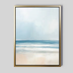 The Blurred Beach Scene Canvas Art - Vertical features a minimal, abstract coastal print of ocean, sky, and sand in soft blue and white tones. The gold frame with a thin black border adds elegance—ideal wall decor for serene beach-inspired spaces.