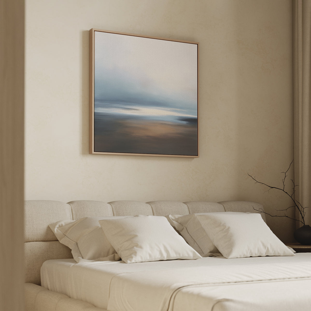 A minimalist bedroom with a beige bed, white bedding, and pillows features the Blurred Seascape Canvas Art - Square above the bed. This framed abstract painting in soft blue, white, and brown tones complements the room’s neutral walls and simple decor.