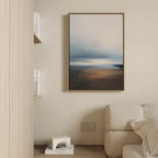 A minimalist living room corner features a beige sofa, a book shelf, a small white geometric decor piece, and the Blurred Seascape Canvas Art - Vertical on the wall for a touch of coastal serenity.