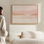 A person stands in a minimalist room facing the Blush Mesa Canvas Art - Horizontal above a cream sofa, creating an inviting earth-toned decor.