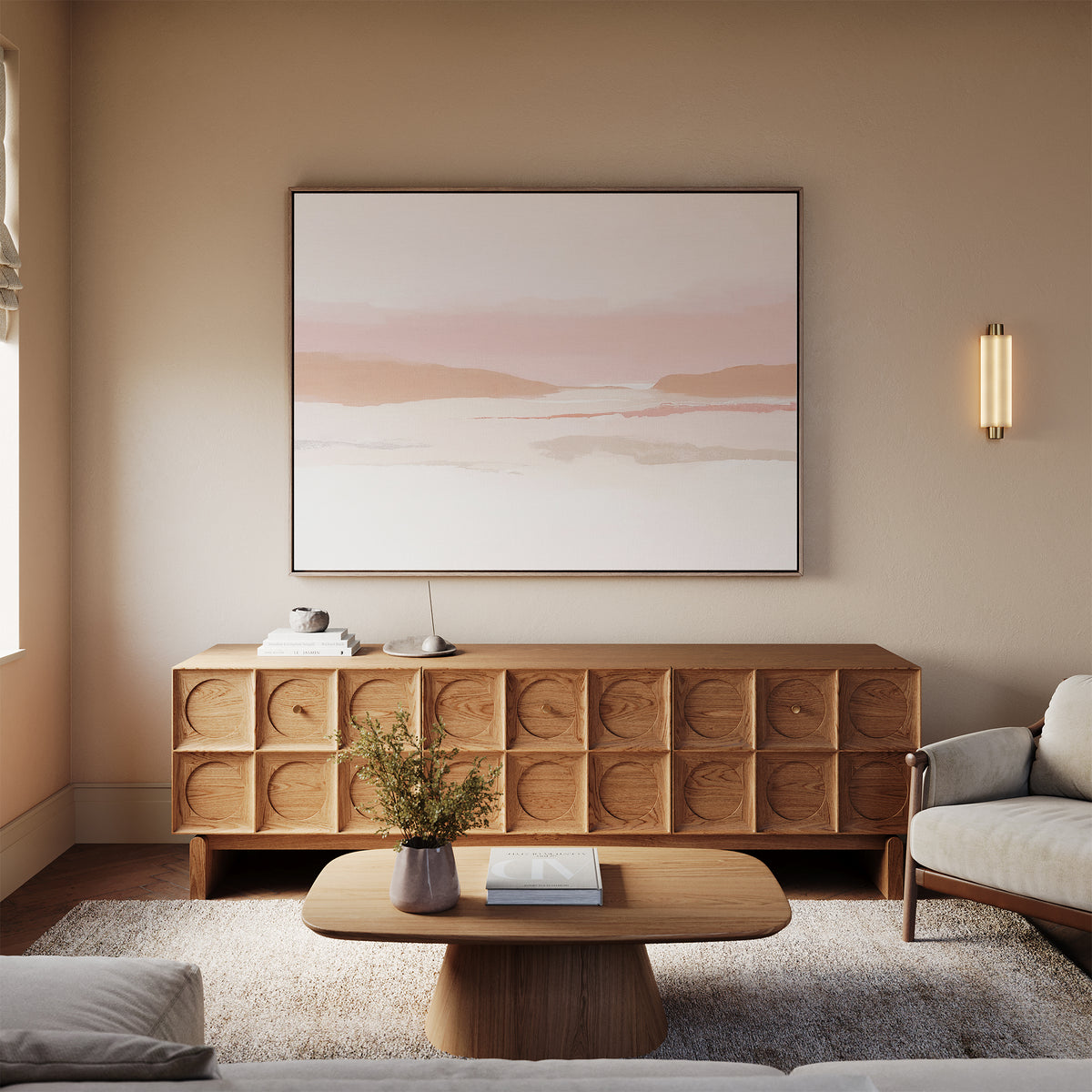 A modern living room with a beige wall, Blush Mesa Canvas Art - Horizontal as minimalist wall art, wooden sideboard with carved doors, oval coffee table, sofa, and a small vase of flowers. Soft natural light enhances the tranquil atmosphere.
