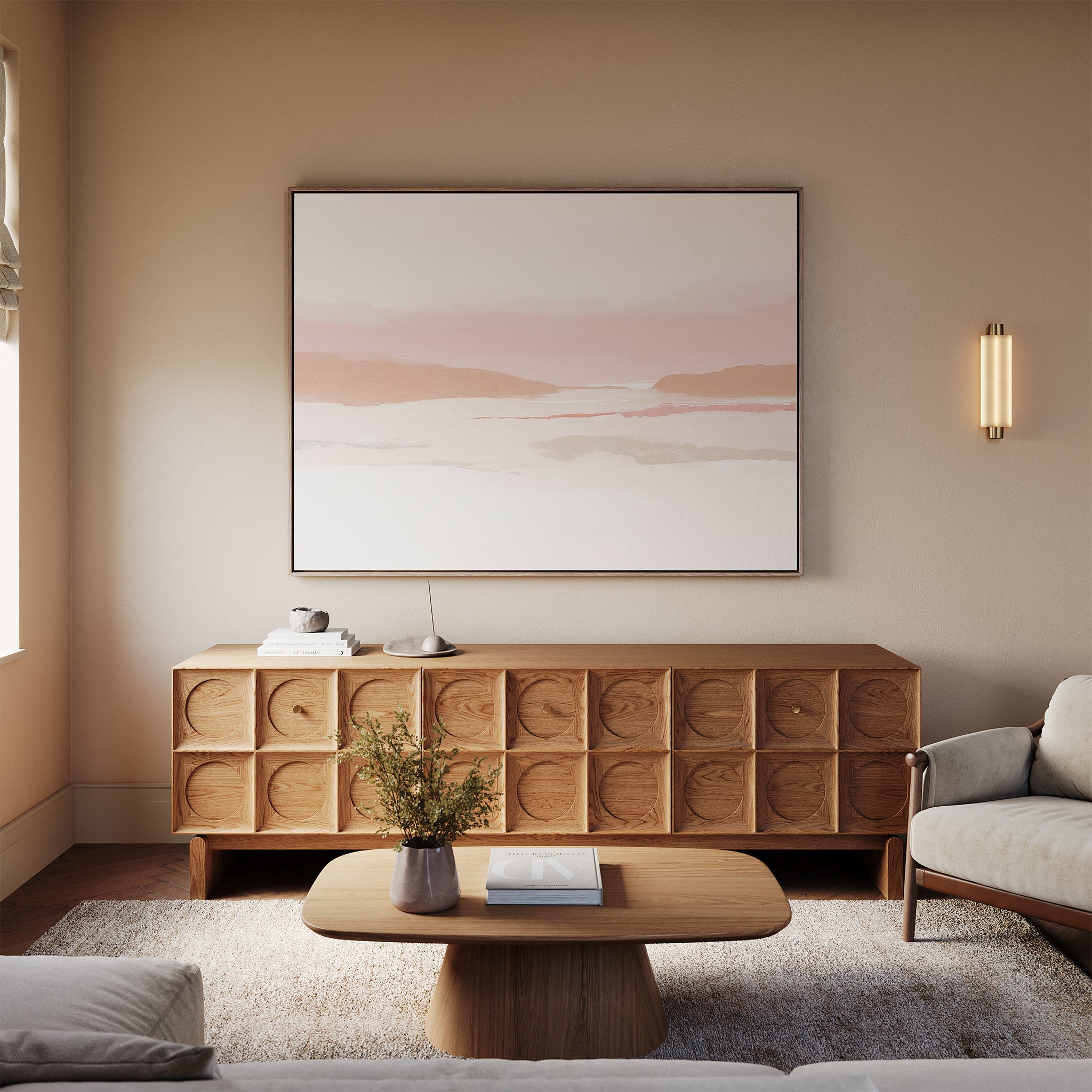 A modern living room with a beige wall, Blush Mesa Canvas Art - Horizontal as minimalist wall art, wooden sideboard with carved doors, oval coffee table, sofa, and a small vase of flowers. Soft natural light enhances the tranquil atmosphere.
