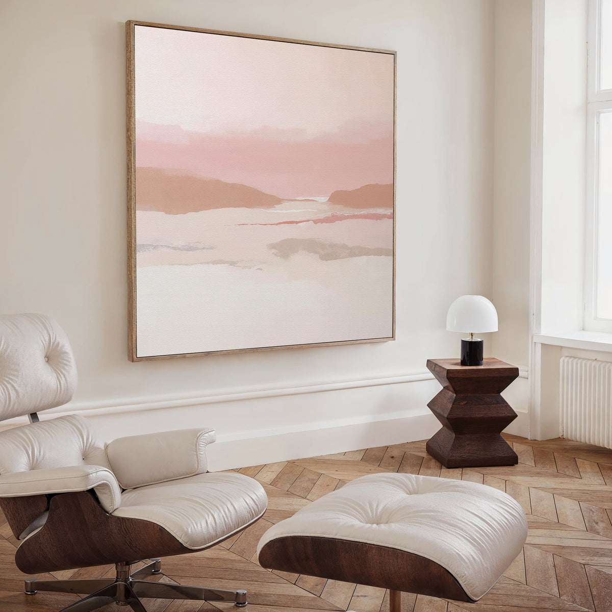 A modern living room with a white leather lounge chair and ottoman, a geometric wooden side table, and earth tones. The Blush Mesa Canvas Art - Square hangs above the light wood herringbone floor by a large window.