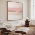 A modern living room with a white leather lounge chair and ottoman, a geometric wooden side table, and earth tones. The Blush Mesa Canvas Art - Square hangs above the light wood herringbone floor by a large window.