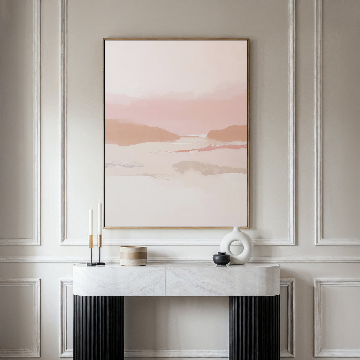 A minimalist console table with decorative objects sits against a paneled wall, topped by the Blush Mesa Canvas Art - Vertical, featuring soft pink, beige, and earth tones for an elegant and serene scene.