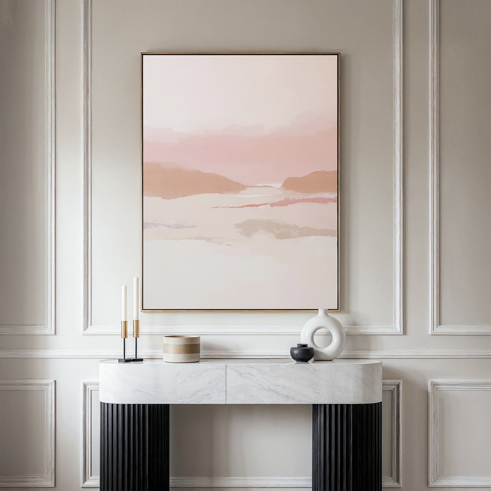 A minimalist console table with decorative objects sits against a paneled wall, topped by the Blush Mesa Canvas Art - Vertical, featuring soft pink, beige, and earth tones for an elegant and serene scene.