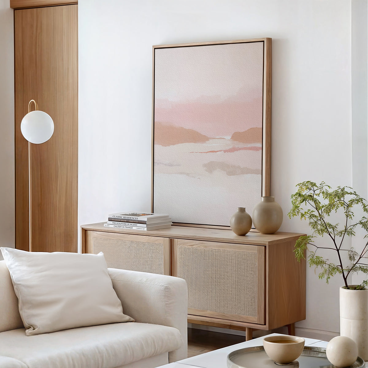 A minimal, modern living room with a light wood sideboard, the vertical Blush Mesa Canvas Art in pastel earth tones, neutral vases, a small plant, and a white couch with a cushion. Soft natural light fills the space.