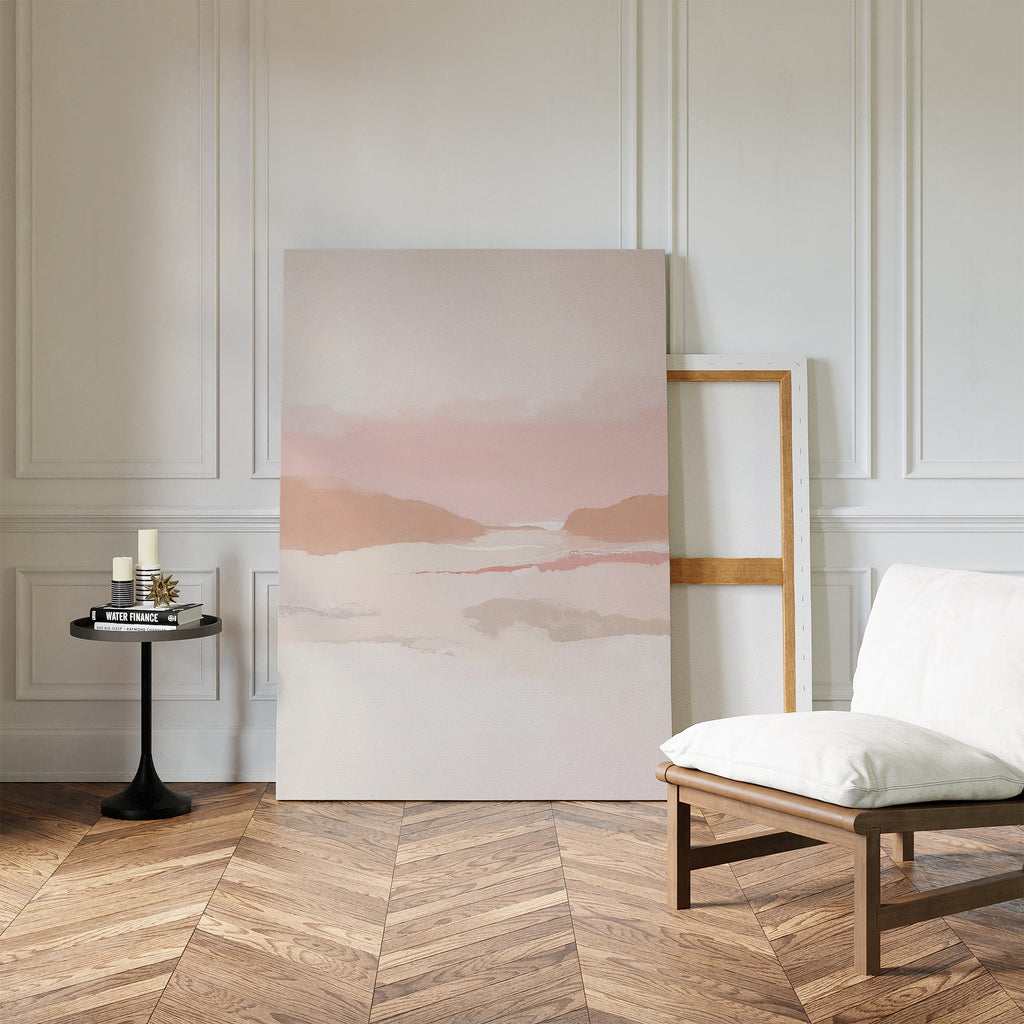 A minimalist room with herringbone wood floors, earth tones, a white cushioned chair, black side table with candles and books, and the Blush Mesa Canvas Art - Vertical leaning against a white paneled wall.