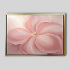 The Blushing Magnolia Canvas Art - Horizontal features a large, soft pink magnolia with delicate petals and a light yellow center on a pale background. Its gold frame with a black inner border adds an elegant touch to any space.