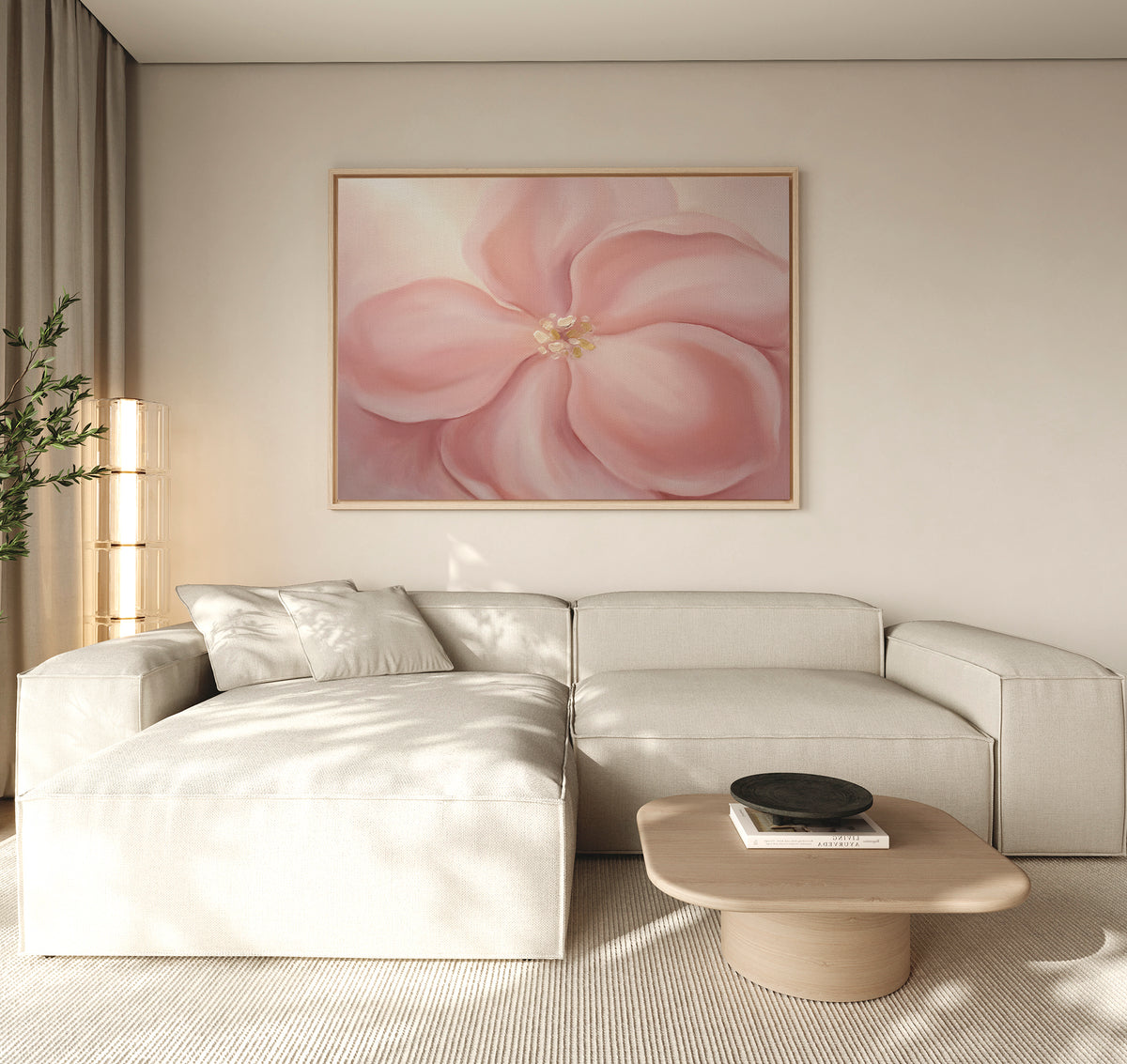 A modern living room features a beige sectional, a light wood coffee table, and the Blushing Magnolia Canvas Art - Horizontal on the wall. Soft neutrals and natural light enhance the calm, minimalist vibe.