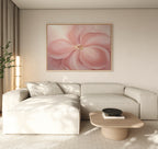 A modern living room features a beige sectional, a light wood coffee table, and the Blushing Magnolia Canvas Art - Horizontal on the wall. Soft neutrals and natural light enhance the calm, minimalist vibe.
