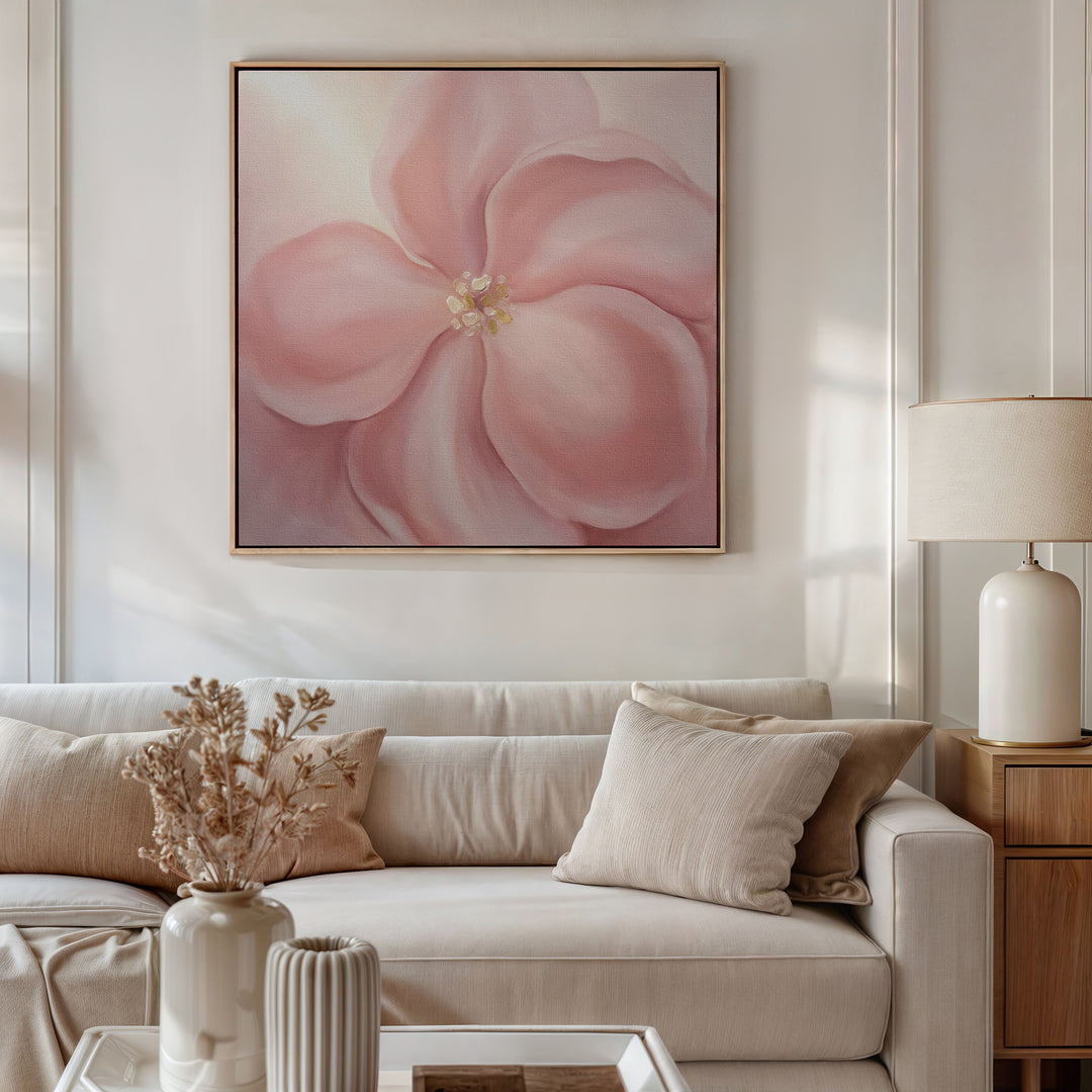 A cozy living room with a cream sofa, beige pillows, a wooden side table and white lamp, dried flowers in a vase, and the Blushing Magnolia Canvas Art - Square fills the space with warmth and a touch of romance.
