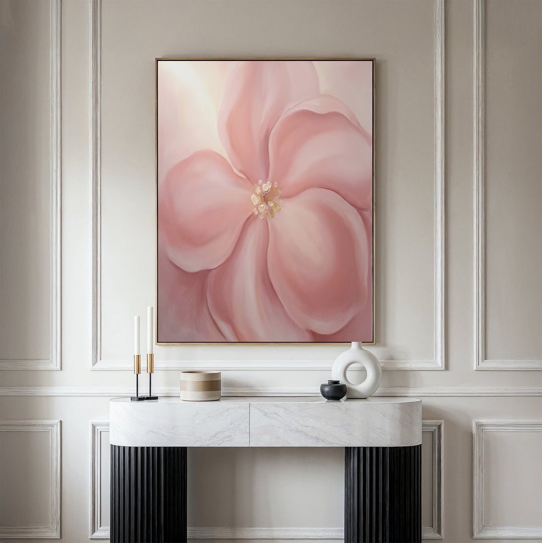 The Blushing Magnolia Canvas Art - Vertical hangs on a beige paneled wall above a white marble console table with black legs, styled with candles, a round vase, and a wooden box for soft romantic wall art appeal.